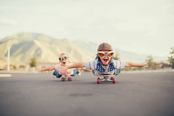 Young Boy and Girl Imagine Flying On Skateboard A young boy and girl are wearing flying goggles while outstretching their arms to attempt flying while on skateboards. They have large smiles and are imagining taking off into the sky. championship photos stock pictures, royalty-free photos & images