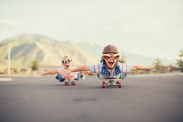 Young Boy and Girl Imagine Flying On Skateboard A young boy and girl are wearing flying goggles while outstretching their arms to attempt flying while on skateboards. They have large smiles and are imagining taking off into the sky. skating stock pictures, royalty-free photos & images