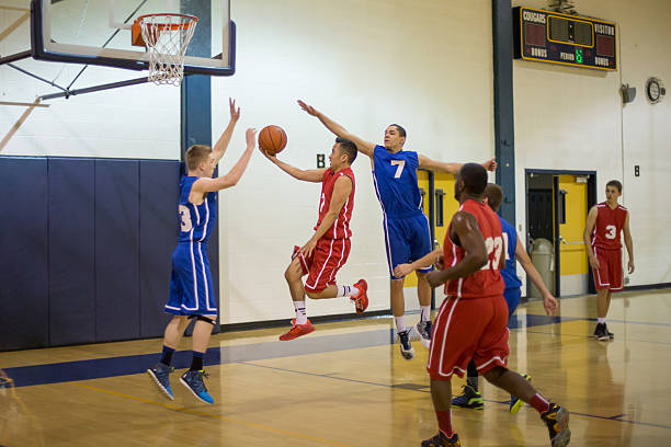 Teenagers playing basketball in gymnasium Teenagers playing high school basketball in gymnasium youth basketball indoor stock pictures, royalty-free photos & images