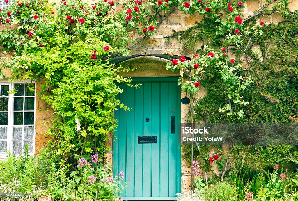 Charming House with green doors and red roses Green wooden doors in an old traditional English stone cottage surrounded by climbing red roses and flowers Cottage Stock Photo
