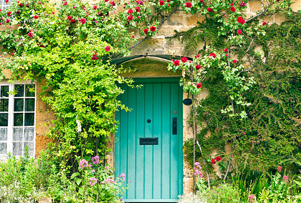 Charming House with green doors and red roses Green wooden doors in an old traditional English stone cottage surrounded by climbing red roses and flowers charming stock pictures, royalty-free photos & images