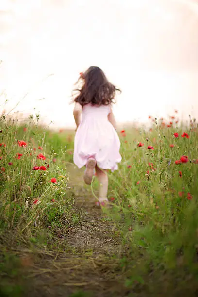 Little girl running away in a field outdoors. Abstract concept of kid wearing a dress running away from camera among poppies.