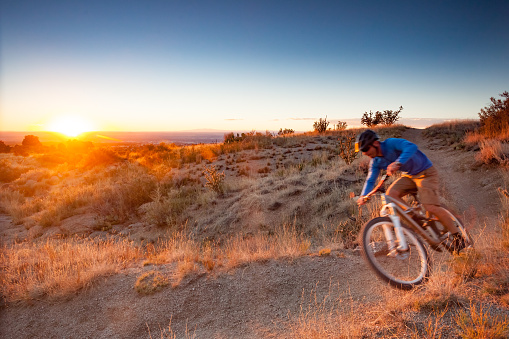 a man speeds by on his mountain bike in the desert landscape as the sunest hits the horizon.  horizontal wide angle composition taken in albuquerque, new mexico.