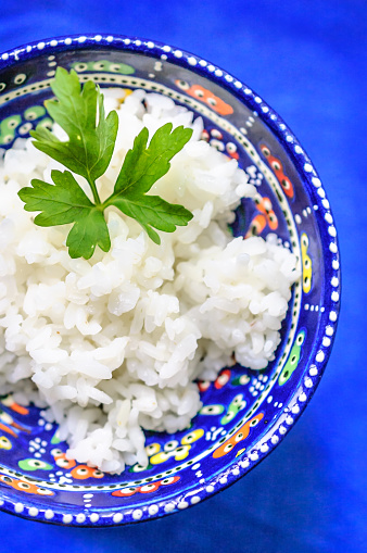 Cooked rice in ethnic bowl on blue background.