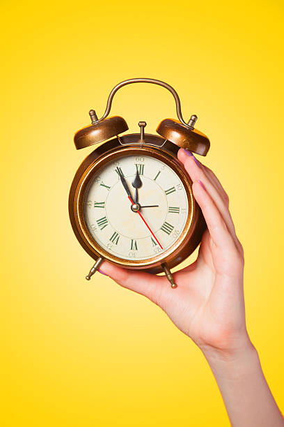 istock Hand holding alarm clock on yellow background. 495757475