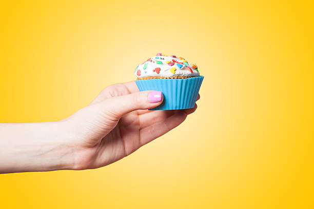 istock Hand holding cupcake on yellow background 495757477