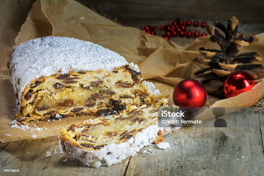 Christmas stollen, traditional German cake in brown paper on rus Christmas stollen, traditional German cake typical in Dresden for Advent and Christmas season, pine cones and red baubles as decoration, in brown paper on a rustic wooden board. 2015 Stock Photo