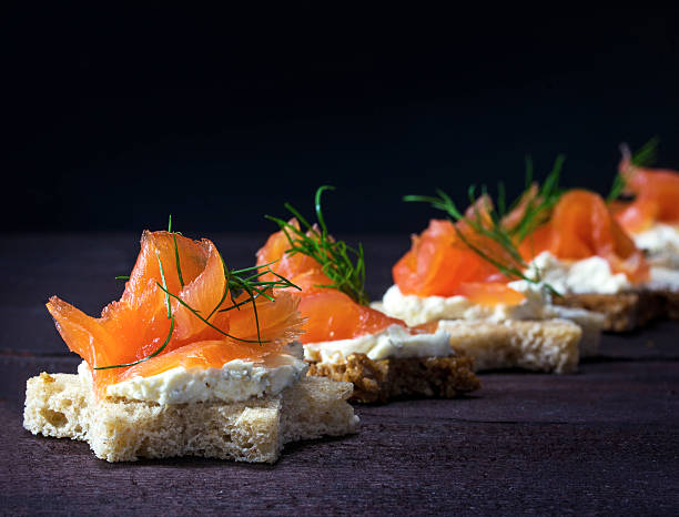 canapes in star shape with salmon on dark wood Row of festive canapes in star shape with smoked salmon for Christmas or New Year on a dark wooden background, selected focus, narrow depth of field smoked salmon stock pictures, royalty-free photos & images