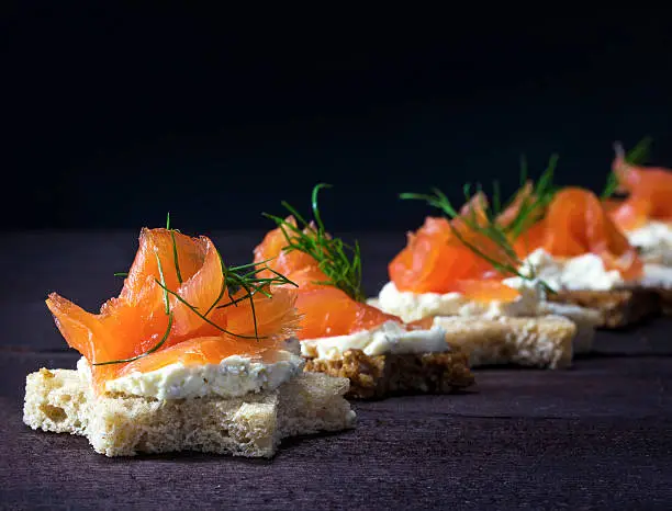 Row of festive canapes in star shape with smoked salmon for Christmas or New Year on a dark wooden background, selected focus, narrow depth of field