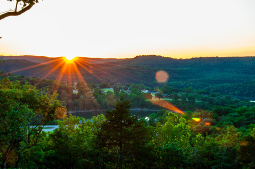 Eureka Springs Sunset over the hill country in the Ozark Mountains the sun sets behind the Ridge and a large Lens Flare pops into view a coloful orange glowing star