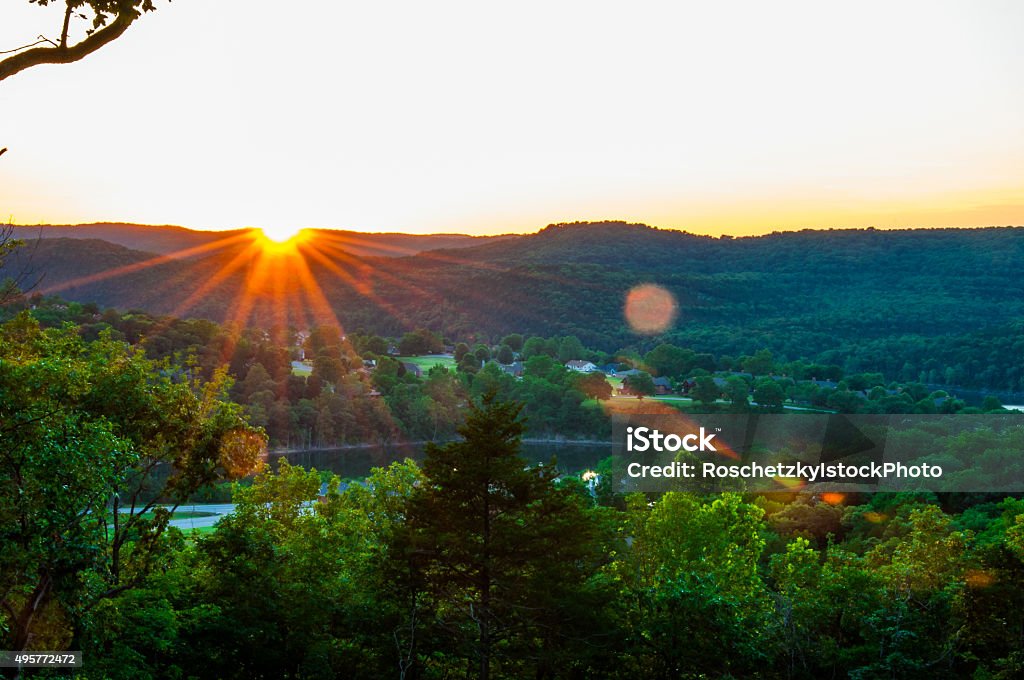 Eureka Springs Sunset Eureka Springs Sunset over the hill country in the Ozark Mountains the sun sets behind the Ridge and a large Lens Flare pops into view a coloful orange glowing star Ozark Mountains Stock Photo