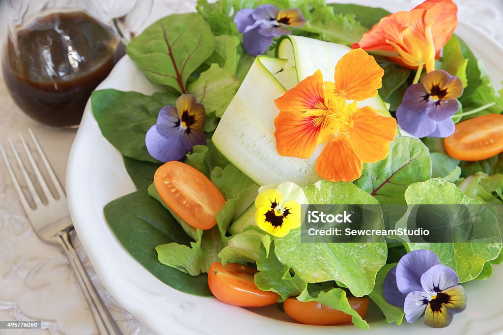 Fresh green salad with edible flowers Fresh green salad with edible flowers in white serving dish 2015 Stock Photo