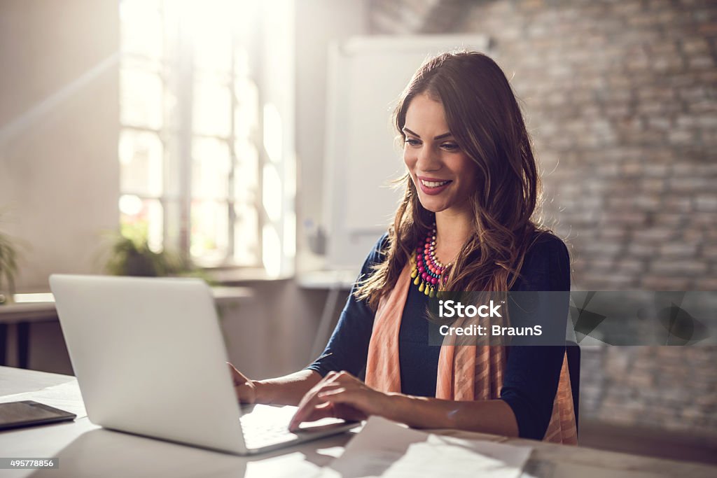 Young happy businesswoman working on laptop in the office. Happy businesswoman sitting in the office and working on computer. Laptop Stock Photo