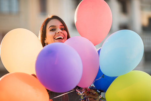 Young happy woman peeking behind group of colorful balloons.