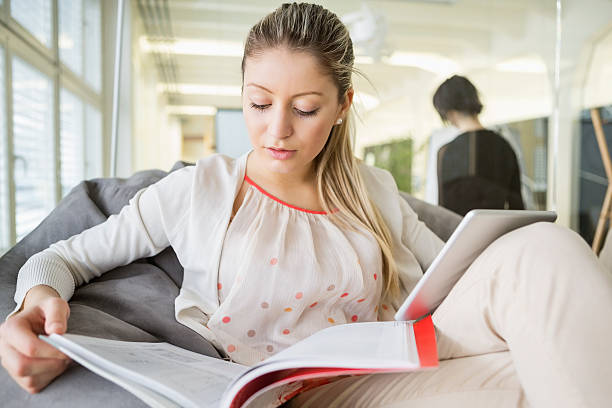 istock Young businesswoman with digital tablet reading book in office 495783245