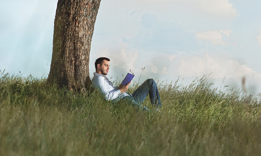 Young man read book and repose on grass. Outdoors