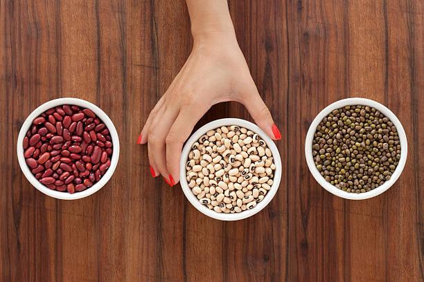 Offering beans Top view of three bowls containing bean varieties and one woman hand holding the one in the middle organic red cowpea beans stock pictures, royalty-free photos & images