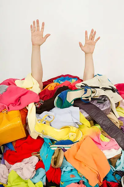 Man hands reaching out from a big pile of clothes and accessories. Man reaching for help from to much woman shopping.