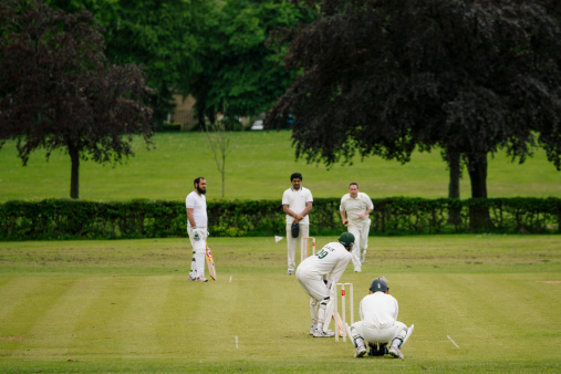 Focus on cricket wicket. Male friends and family members playing cricket together out of focus in the background together on a sunny day in Northumberland.