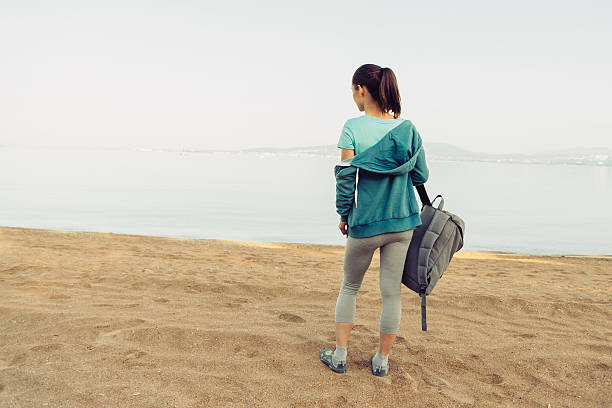 istock Sporty girl with backpack standing on beach 495826872