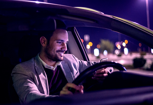 Portrait of a young man having phone conversation in his car.Man using smart phone.Driving a car at night -man driving his modern car at night in a city.