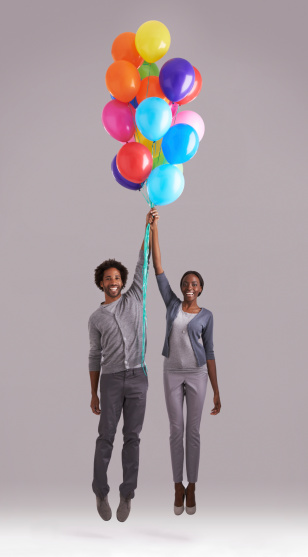 Studio shot of a young couple holding a bunch of balloons as they float away