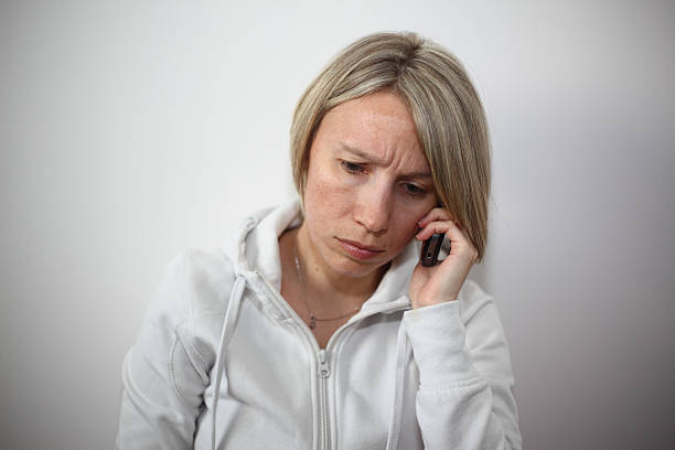 A close up image of a young woman sitting near the wall talking on the cell phone with a sad and worried look on her face. See more in my portfolio.