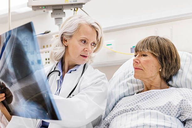 Mature Female Doctor Checking X-Ray With Mature Patient Mature female doctor checking x-ray with female mature patient in patient room. leanincollection stock pictures, royalty-free photos & images