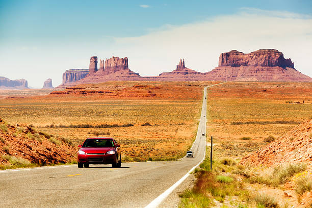 Touring the American Southwest, Monument Valley Highway with Cars Subject: Tourists in a red car traveling in the American Southwest, driving downhill on a straight length of highway stretching from southern Utah toward Monument Valley, Arizona the mittens monument valley stock pictures, royalty-free photos & images