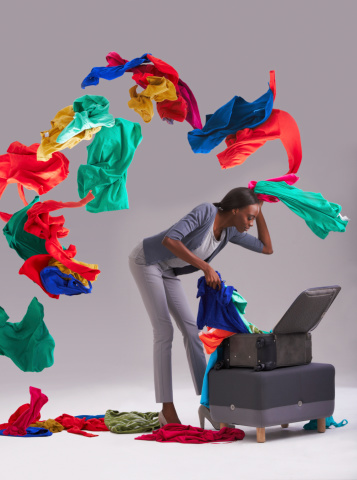 Studio shot of a young woman throwing her multi colored clothes out of a suitcase