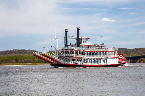 A Paddle wheel riverboat is cruising on the Illinois River as it takes riders along for a ride to view the scenic river and nature are Peoria, Illinois