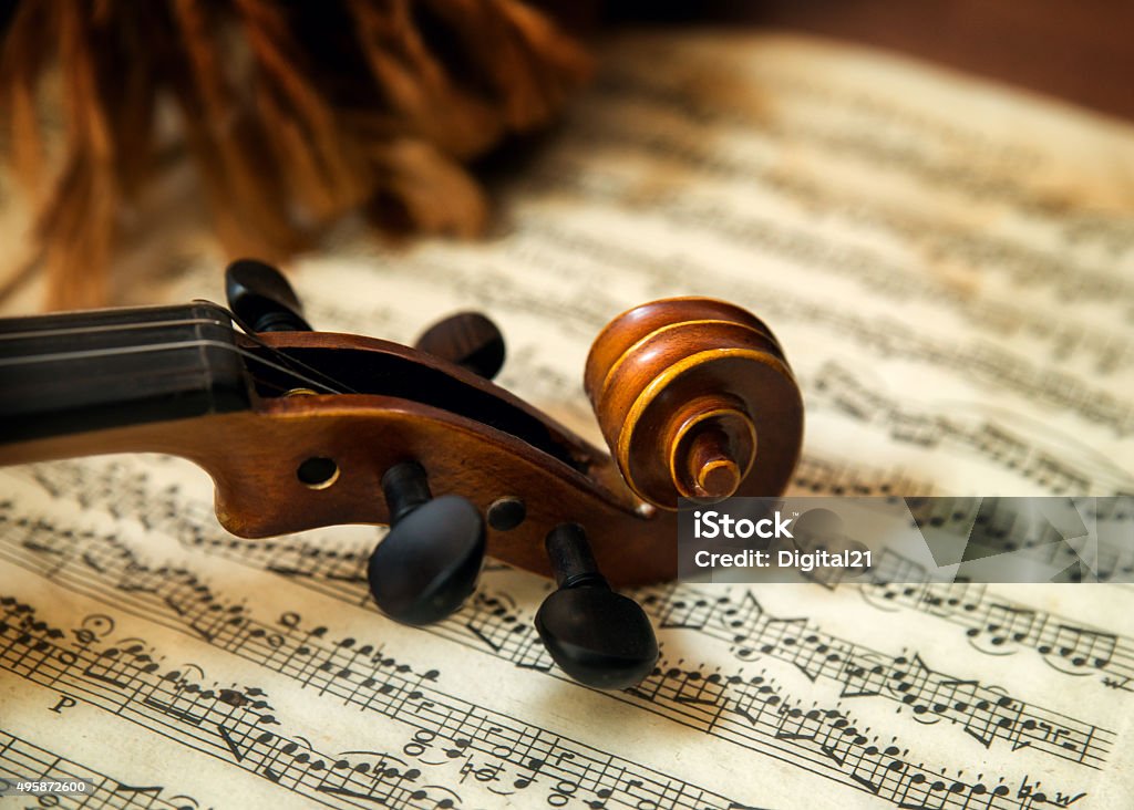 Violin head on sheet music Old wooden string instrument (violin) resting on classical sheet music. Focus is on the scroll, tuning pegs, and part of the neck. Classical Music Stock Photo