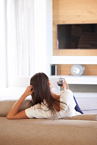 Shot of a young woman changing channels with a remote control while relaxing on the couch