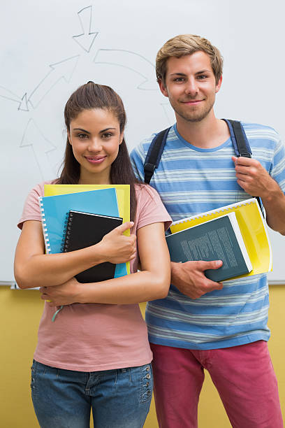 istock Attractive students smiling at camera in front of whiteboard 495874977