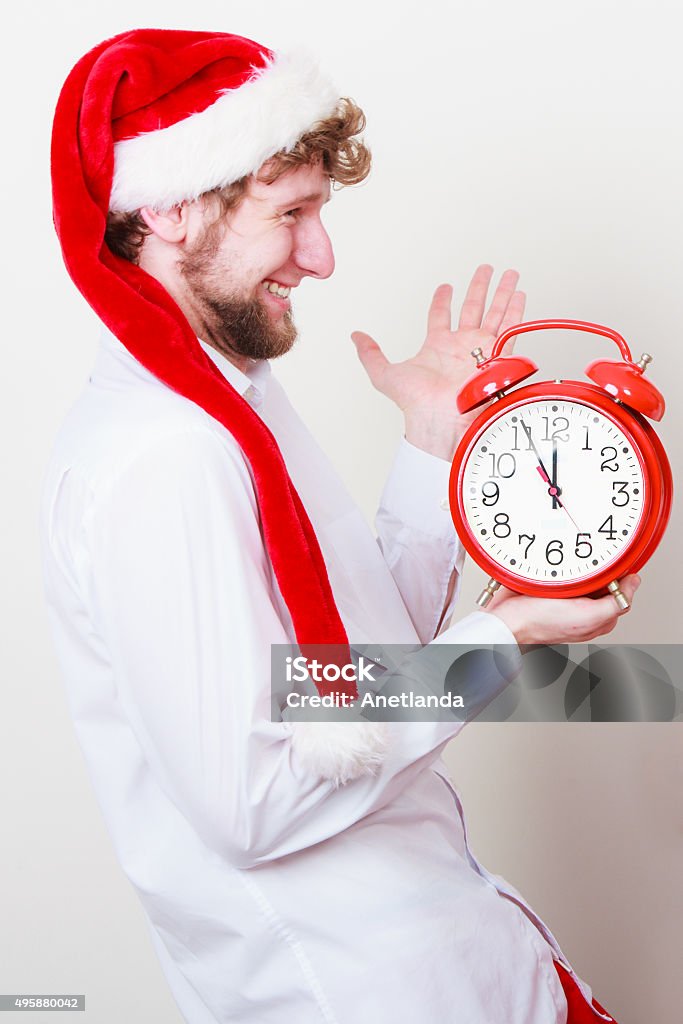 Happy man with alarm clock. Christmas time. Happy man in santa claus hat holding alarm clock on gray. Christmas time season concept. 12 O'Clock Stock Photo