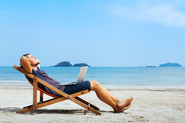 business travel smiling businessman with computer relaxing on the beach deck chair stock pictures, royalty-free photos & images