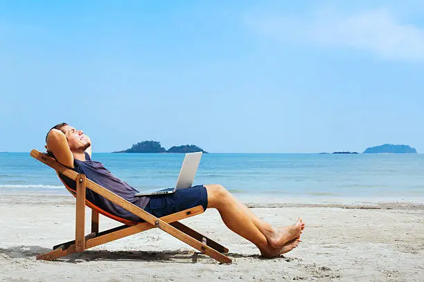 smiling businessman with computer relaxing on the beach