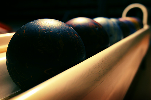 Dark image of bowling balls on rack. Vintage balls showing quite a bit of wear.