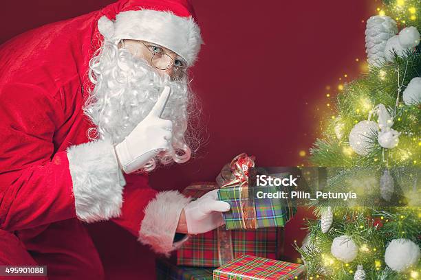 Santa Claus Putting Gift Box Or Present Under Christmas Tree Stock Photo - Download Image Now