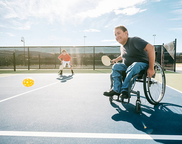 Pickleball Players Two young men playing the game of pickleball on a court. One of the men is in a wheelchair. Horizontal composition with sunlight behind the players. athlete with disabilities photos stock pictures, royalty-free photos & images