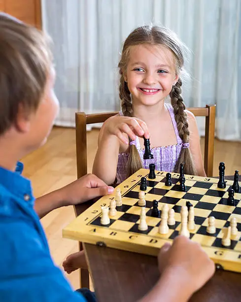 Happy boy and little girl playing chess at home