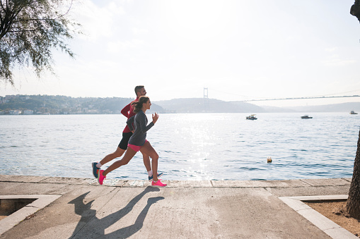 Active energetic couple running together outdoors at the waterfront.
