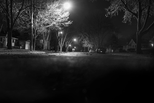 Black and white photograph of street in the United States, with lights illuminating parts of it. Taken at night.
