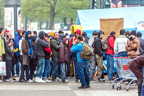 Refugees standing in a row Hamburg, Germany - November 03, 2015: Many refugees standing in a row in Hamburg at the Station. They are waiting for help in front of a tent. refugee camp stock pictures, royalty-free photos & images