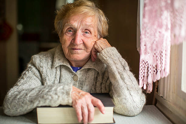 istock Old woman sitting with a book at the table. 495952030