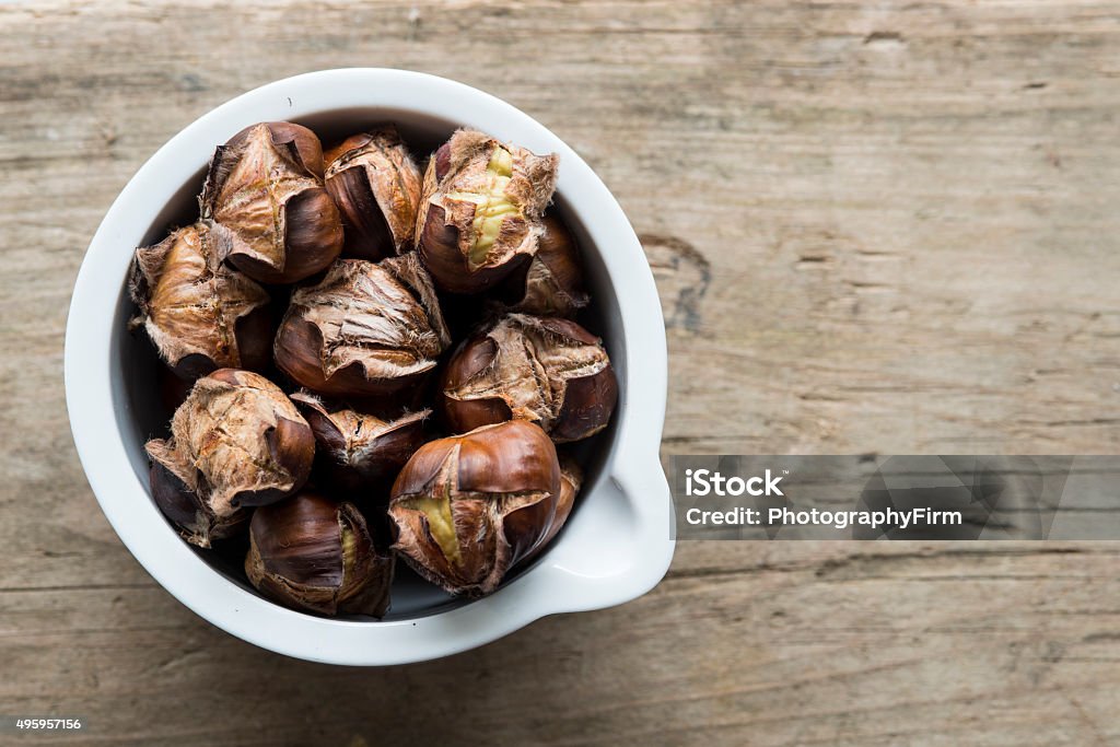 Roast chestnuts in a pot Roast chestnuts in a small white pot on a wooden background 2015 Stock Photo