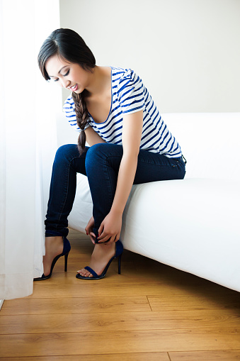 Young beautiful fashion model adjusting her sandal while sitting on sofa.