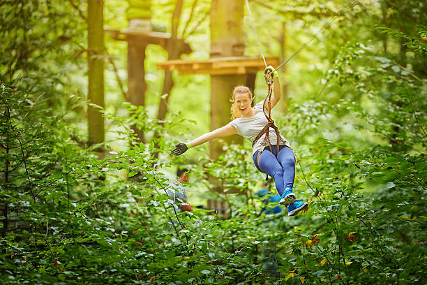 enjoy zipping in forest photo of young woman in adventure park having fun in tyrolean traverse and enjoying her active day.summer season. zip line stock pictures, royalty-free photos & images