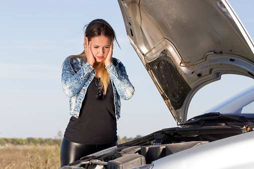 young woman with broken down car on the road