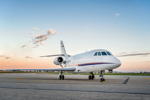 Wide angle view of private luxury business jet parked at the airport asphalt runway, no people image of air vehicle, space for copy. Beautiful blue sky with dusk.